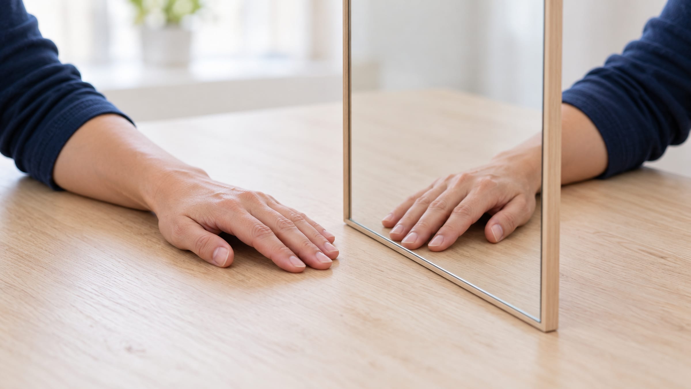 Hände links und rechts eines senkrecht aufgestellten Spiegels auf einem Holztisch
