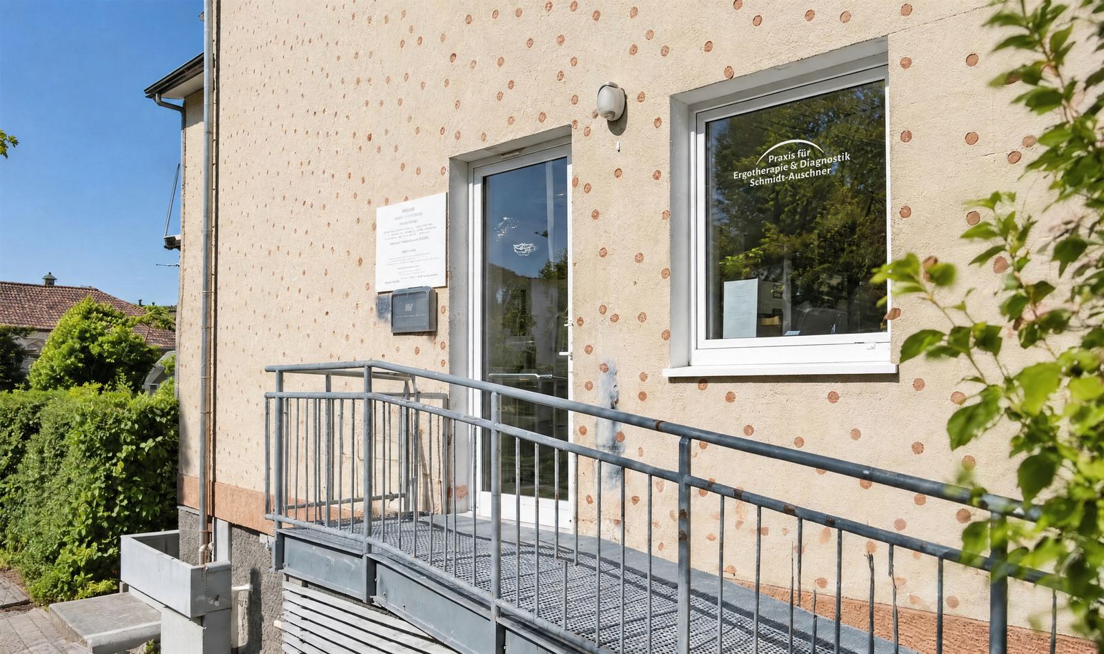 Eingang der Praxis in Iserlohn-Letmathe mit Rampe und dem Praxislogo im Fenster